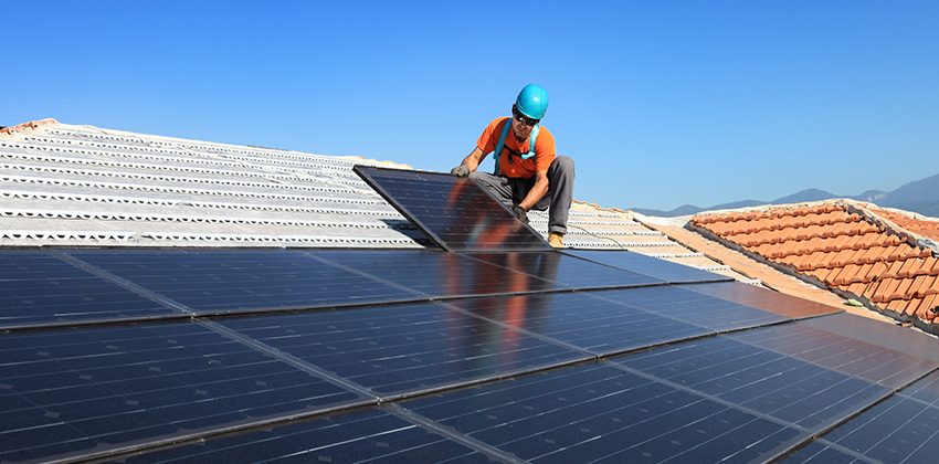 Installer kneeling beside a row of finished solar panels on a sunny roof